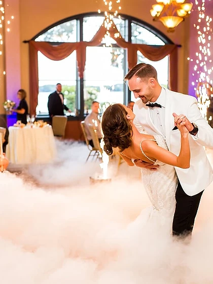 Bride and groom in a dip surrounded by low fog and four cold spark fountains in an elegant ballroom