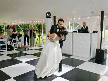 Bride and groom in a dance dip on a checkered dance floor inside the tented pavilion at Geneva On The Lake, with the DJ booth and guests beside them