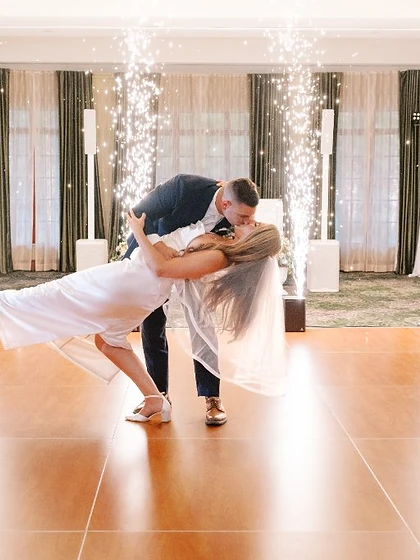 Couple sharing a dip-kiss on the dance floor framed by four vertical sparkler fountains