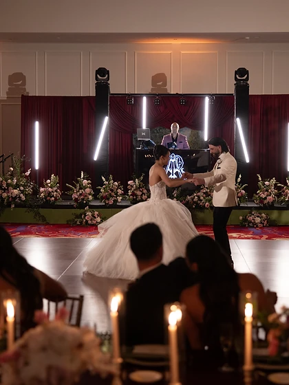 Bride and groom sharing their first dance on a wooden floor with taper candles and a DJ stage behind them