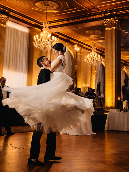 Groom spinning the bride during their first dance in a chandeliered ballroom