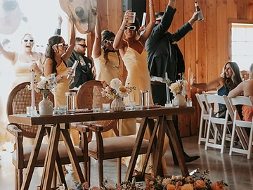 Wedding party gathered behind the head table holding a lit marquee sign and photo props before the bottle service introduction