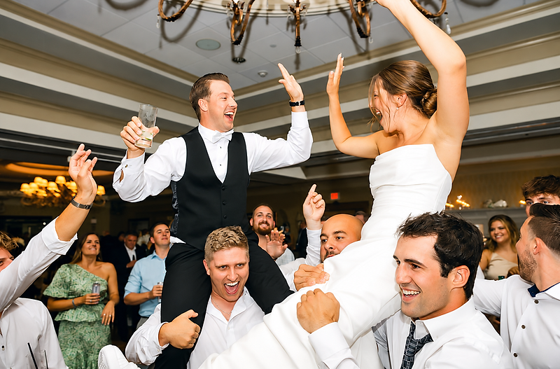 Bride and groom lifted on guests' shoulders during a high-energy wedding reception dance floor celebration