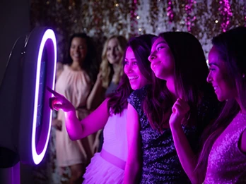 Guests posing at a photo booth with a floral wall and neon sign at a private celebration