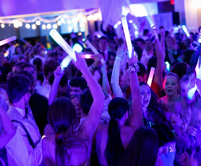 Crowd of students dancing on a prom floor with LED glow sticks under purple and blue lighting