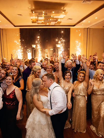 Wedding couple kissing at the center of a cheering crowd with cold sparks behind them