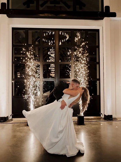 Bride and groom kissing in a dip framed by two cold spark fountains in an industrial venue