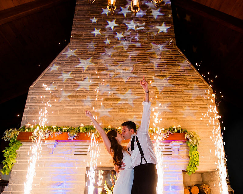 Wedding couple kissing in front of a stone fireplace framed by cold sparks and a star projection