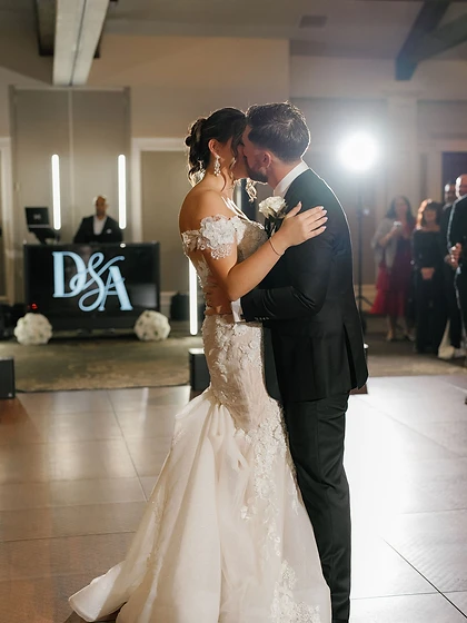 Bride and groom embracing near a monogrammed DJ booth during their wedding reception