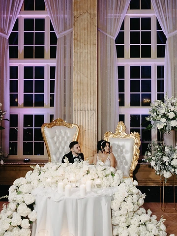 Svetlana and Konstantin seated at their sweetheart table with lush florals and candles in the Grand Ballroom