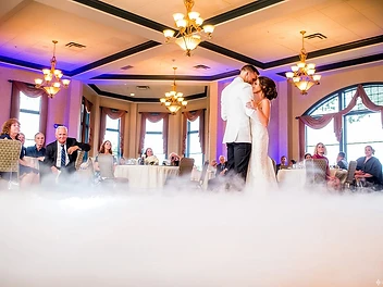 Bride and groom sharing a first dance surrounded by dancing-on-the-clouds fog beneath crystal chandeliers at a Geneva, NY wedding reception