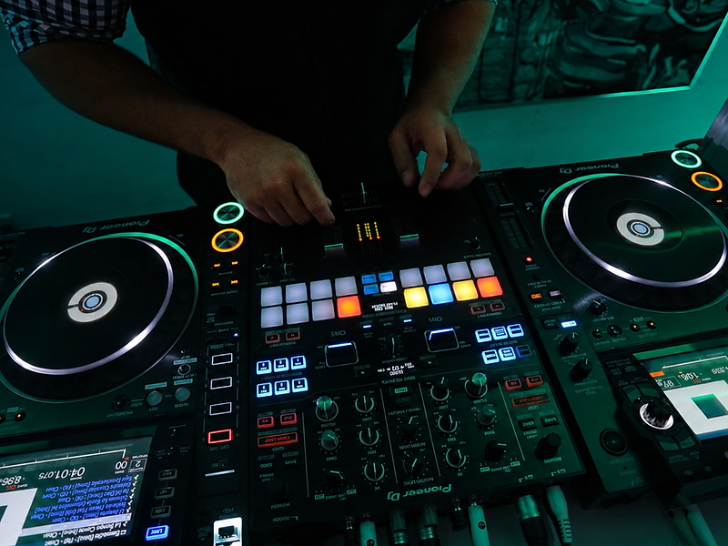 DJ's hands operating a Pioneer controller under teal lighting
