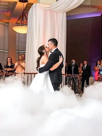 Bride and groom sharing a first-dance kiss surrounded by low-lying fog beneath a draped canopy