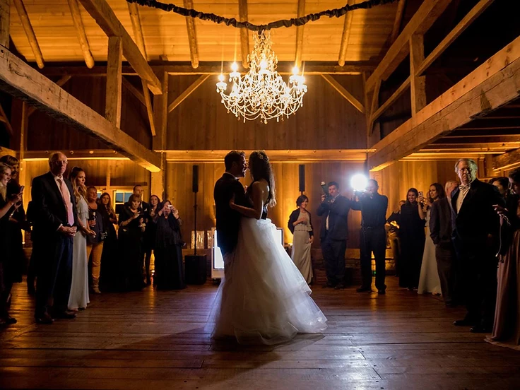 Bride and groom's first dance in a rustic barn with warm uplighting and a crystal chandelier
