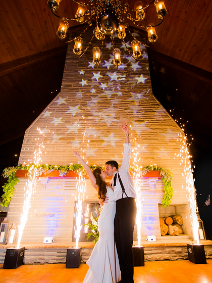 Couple kissing by a stone fireplace surrounded by cold spark fountains at a rustic wedding