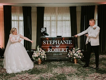 Bride and groom posing in front of their personalized DJ booth with floral arrangements at their Shenandoah Clubhouse wedding at Turning Stone