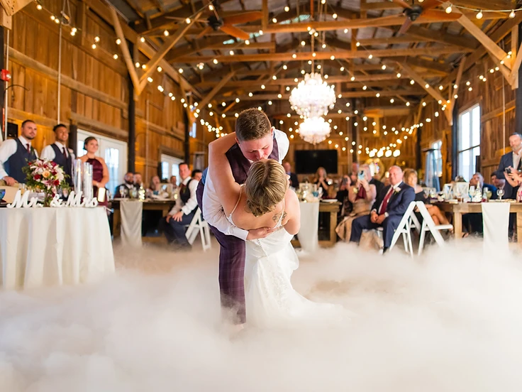 Bride and groom dipping during their first dance surrounded by low-lying clouds in a rustic barn