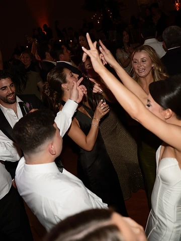 Bride with arms raised dancing with guests on a packed dance floor at a Turning Stone wedding reception in the Oneida Room