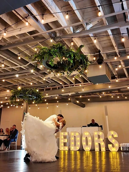 Groom dipping the bride on the dance floor beside a light-up marquee sign at a wedding reception
