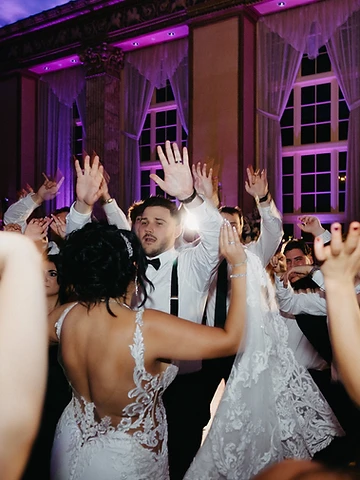 Svetlana and Konstantin dancing with arms raised as guests join hands around them under magenta uplighting
