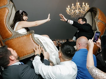 Bride and groom lifted in chairs by their guests during a chair dance inside the tent at Geneva On The Lake