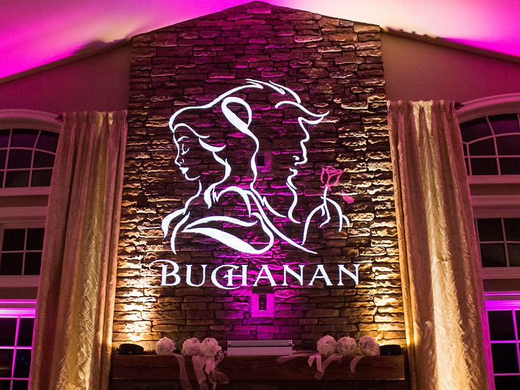 Projection mapping on a stone fireplace showing silhouettes and a custom name, framed by magenta uplighting