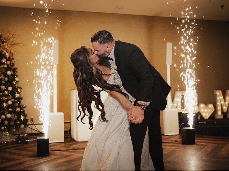 Wedding couple in a dip kiss framed by twin fountains of cold sparks