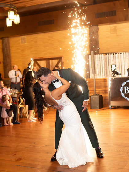 Groom in a green tux dipping the bride as a sparkler fountain fires beside them at a wedding reception
