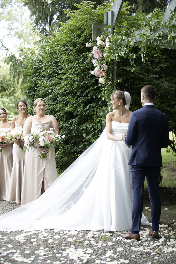 Bride and groom exchanging vows under a flower-covered arbor during their John Joseph Inn wedding ceremony in Groton, near Ithaca