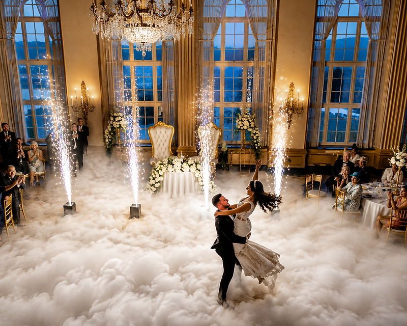 Bride and groom dancing on a cloud of low-lying fog surrounded by four cold spark fountains in a grand ballroom