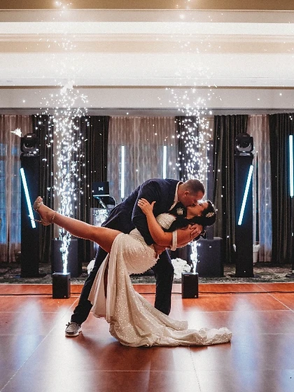 Couple in a dip-kiss framed by four sparkler fountains with blue stage lighting at a wedding reception