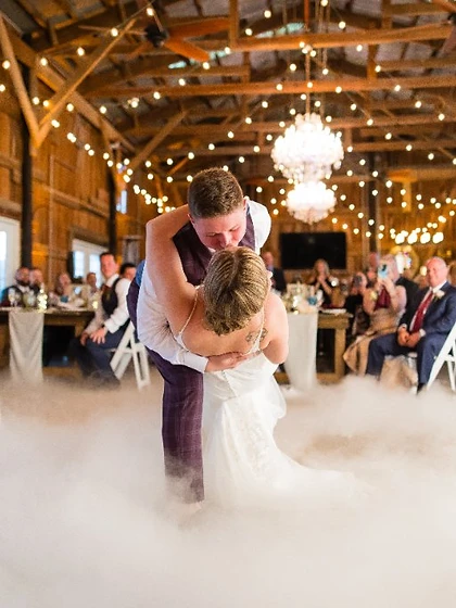 Bride and groom in a dip on a low-fog dance floor beneath string lights at a rustic farmhouse wedding