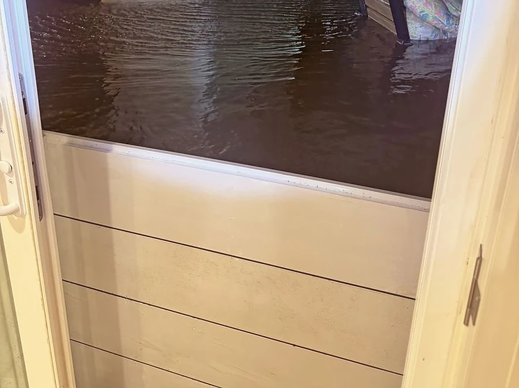 View through doorway showing floodwater outside while inside stays dry, protected by Fortress aluminum barrier