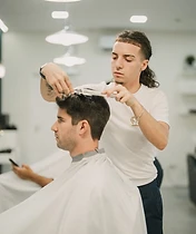 Barbeiro a aparar cabelo com máquina, reflexo no espelho