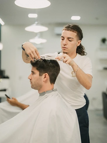 Barbeiro a aparar cabelo com máquina, reflexo no espelho