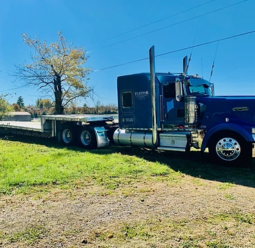 Blue Kenworth semi-truck with a silver flatbed trailer on a sunny day