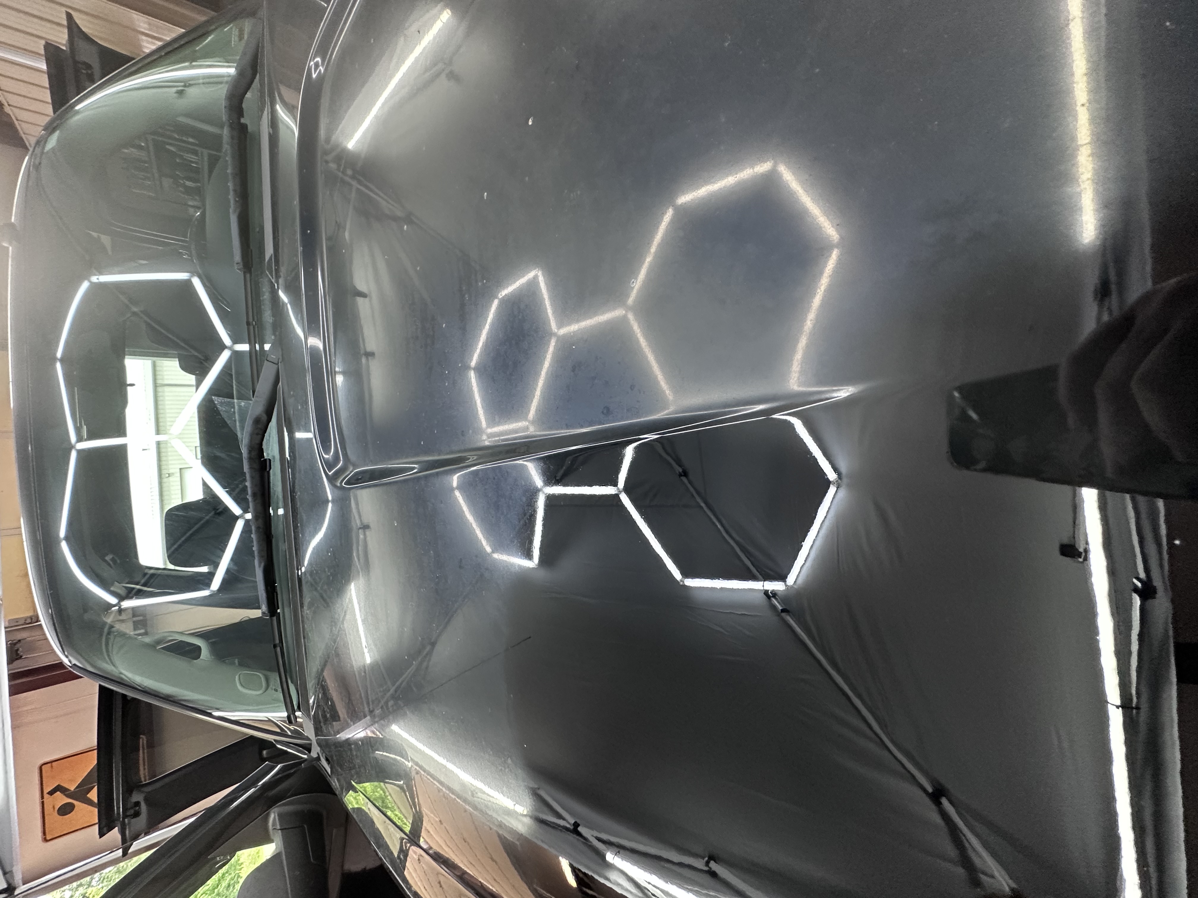 Dark vehicle hood reflecting hexagonal LED workshop lights after paint correction