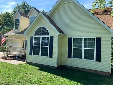 Pale yellow vinyl-sided home with navy shutters and a green lawn, exterior washed clean by A&P Wash Services
