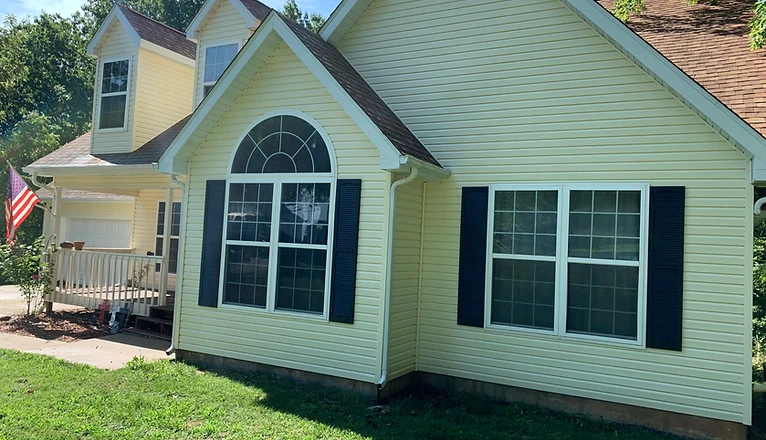 Pale yellow vinyl-sided home with navy shutters and a green lawn, exterior washed clean by A&P Wash Services