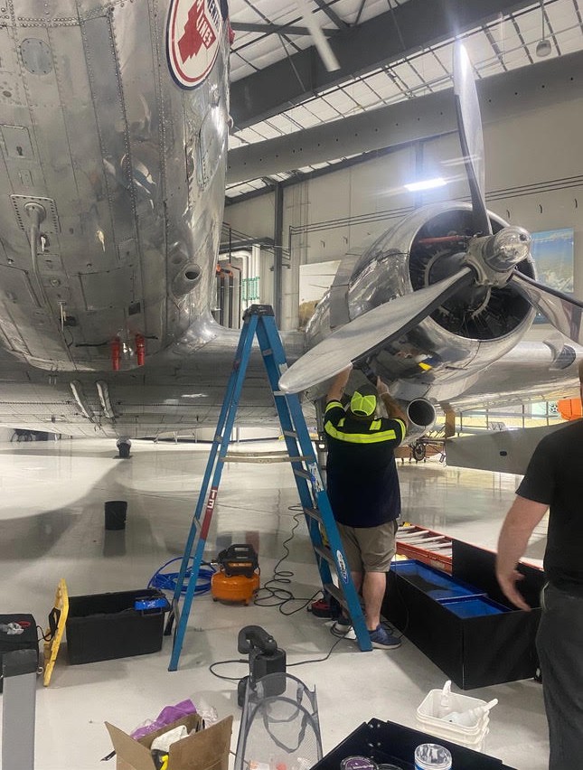 A&P Wash Services technician servicing a polished vintage twin-engine aircraft inside a maintenance hangar