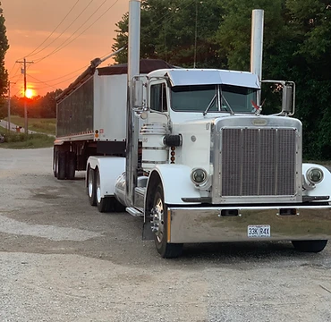 White Peterbilt semi-truck with chrome detailing parked on a gravel lot at golden sunset
