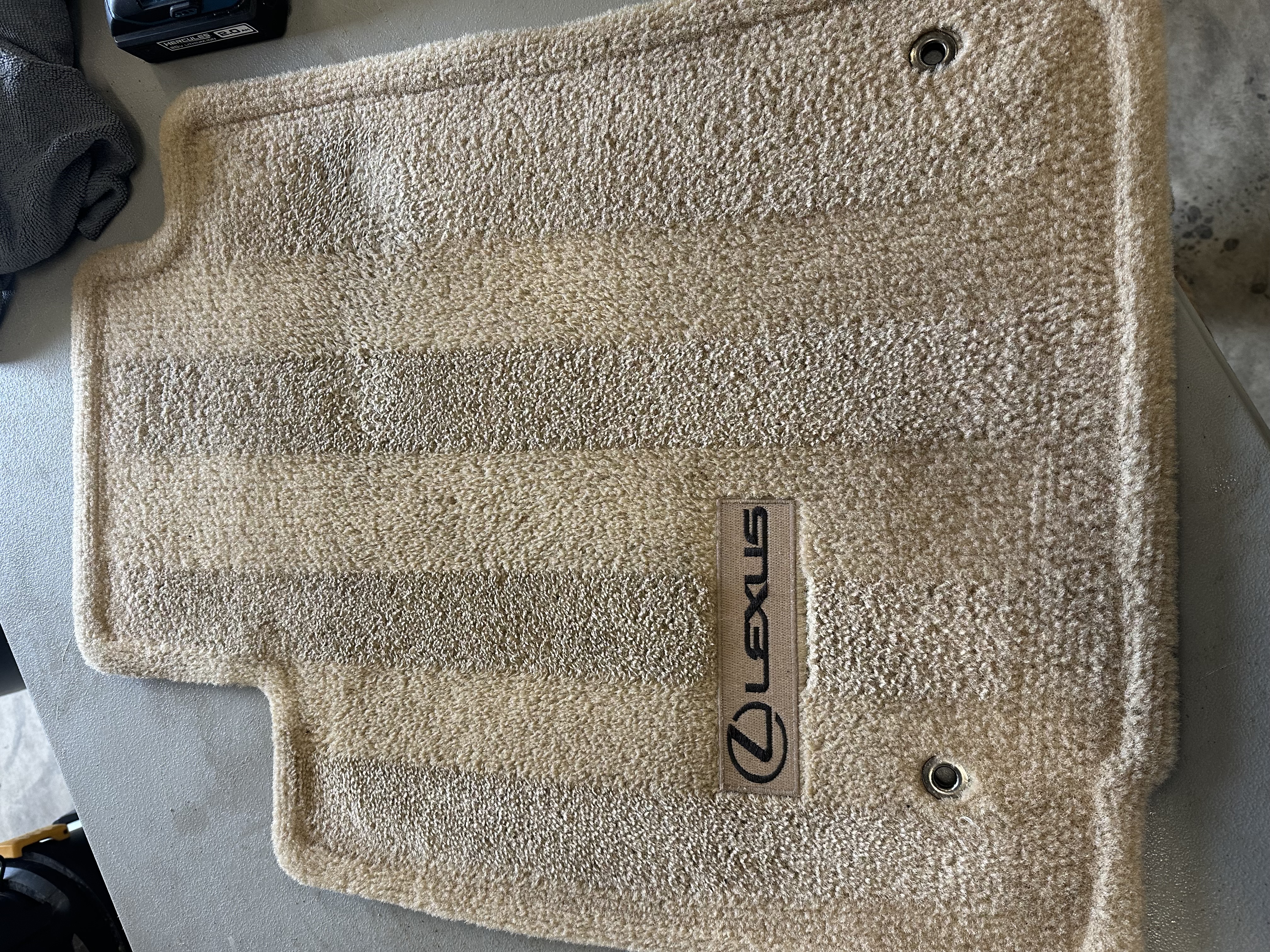 Tan carpeted Lexus floor mat with branded Lexus logo inlay after cleaning by A&P Wash Services