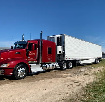 Red Kenworth semi-truck with a white Thermo King refrigerated trailer parked on a gravel lot