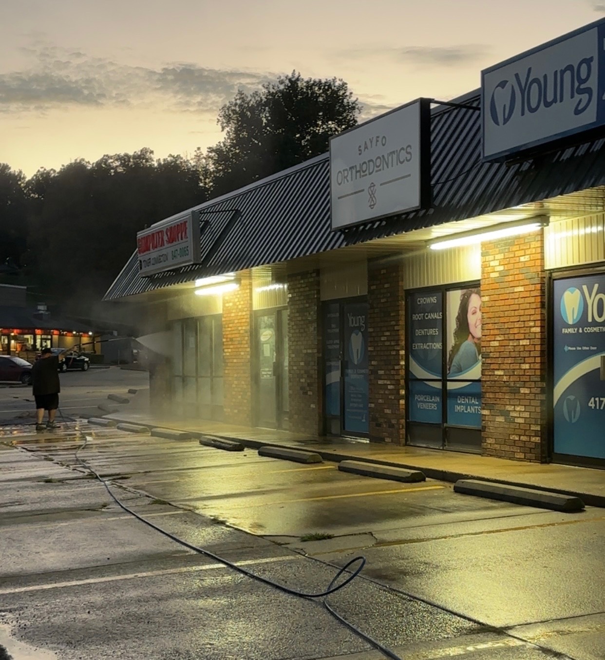 A&P Wash Services pressure washing a commercial storefront parking lot at dusk