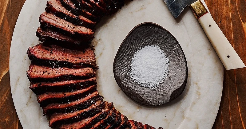 Sliced grilled meat with coarse salt on a marble platter