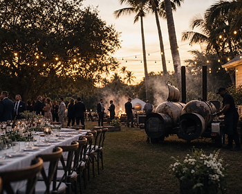 Live-fire smoker and banquet table at an outdoor wedding venue