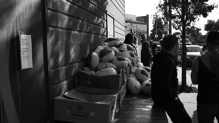 Volunteers and a chef distributing Butterball turkeys at the West Oakland giveaway, with a sign about the relocated location