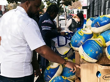 A chef in a white coat handing out turkeys beside crates of water