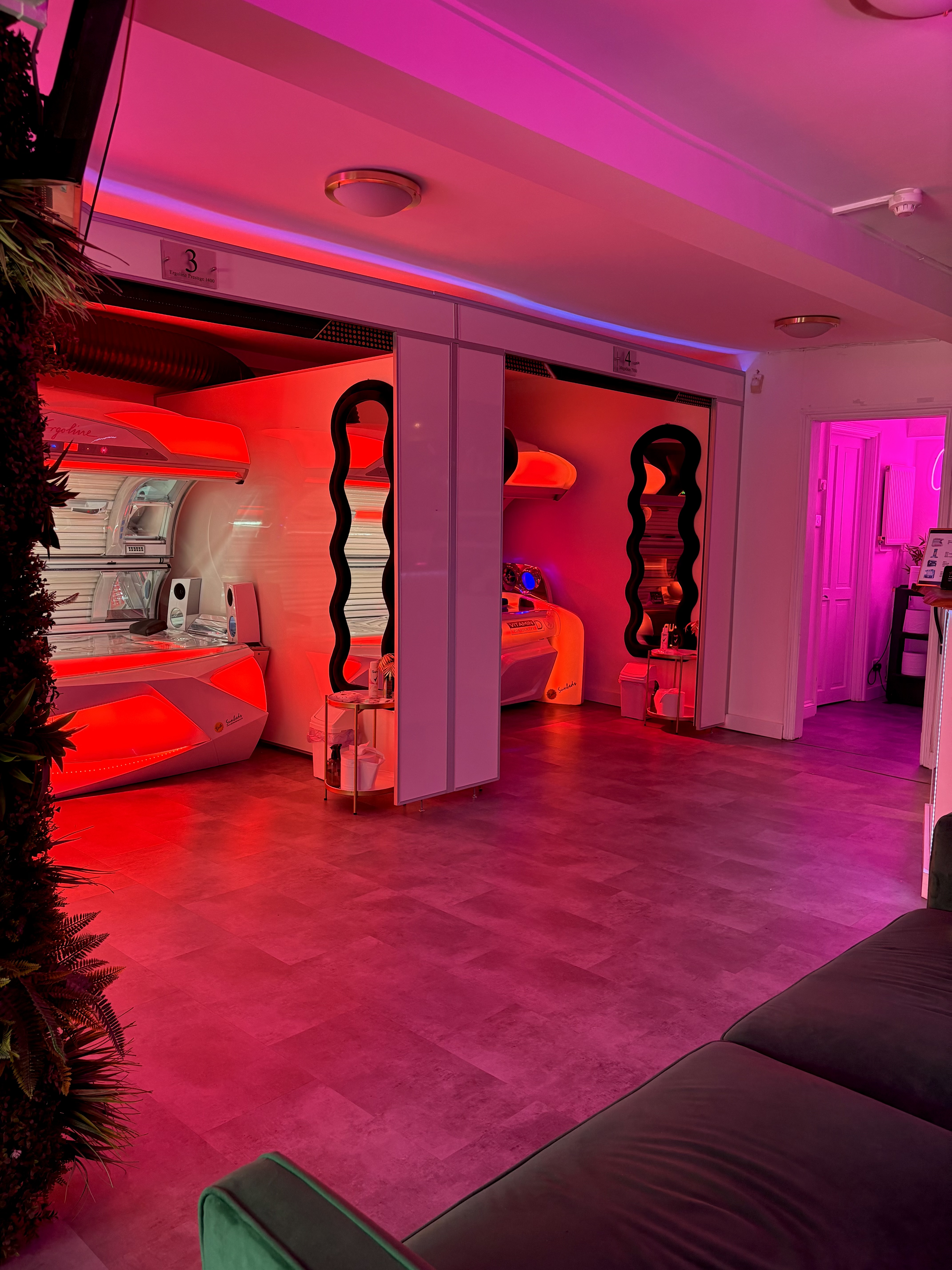 A moody tanning salon interior with glowing Ergoline sunbeds bathed in magenta light