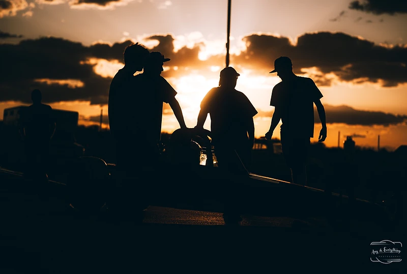 Race crew members silhouetted by sunset in the Top Gun Dragstrip pits